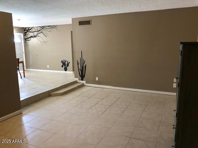 spare room with visible vents, baseboards, a textured ceiling, and light tile patterned flooring