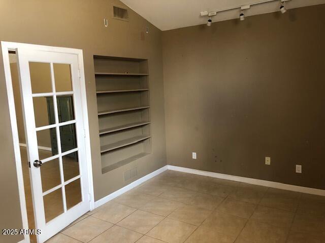 empty room featuring tile patterned flooring, built in shelves, baseboards, and vaulted ceiling