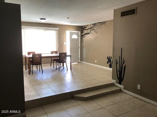 foyer entrance with light tile patterned floors, visible vents, baseboards, and a textured ceiling