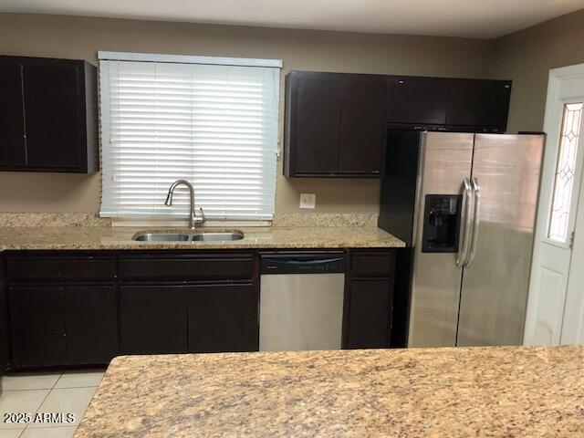 kitchen featuring dark cabinetry, light tile patterned floors, plenty of natural light, a sink, and appliances with stainless steel finishes