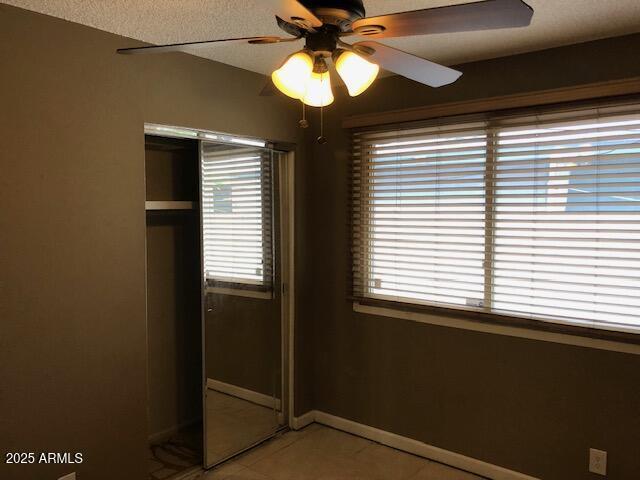 unfurnished bedroom featuring light tile patterned floors, baseboards, multiple windows, and ceiling fan