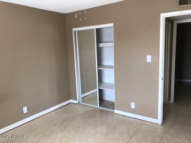 unfurnished bedroom with light tile patterned floors, baseboards, visible vents, and a closet