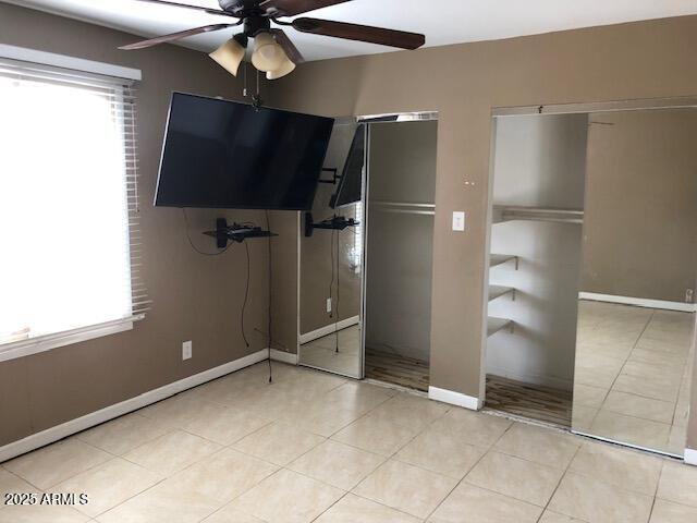 unfurnished bedroom with light tile patterned floors, ceiling fan, baseboards, and multiple closets