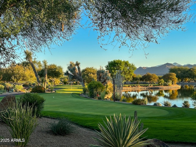 view of community with view of golf course, a lawn, and a water and mountain view