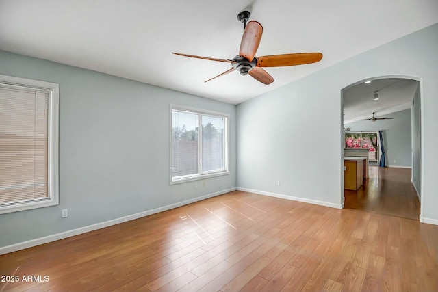 unfurnished room with baseboards, arched walkways, ceiling fan, and wood finished floors