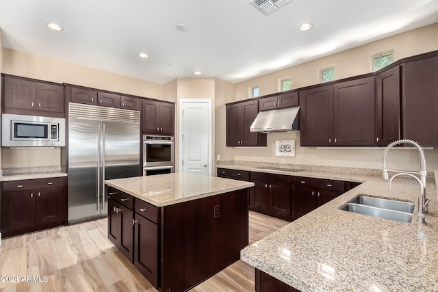 kitchen with light stone countertops, dark brown cabinetry, built in appliances, and sink