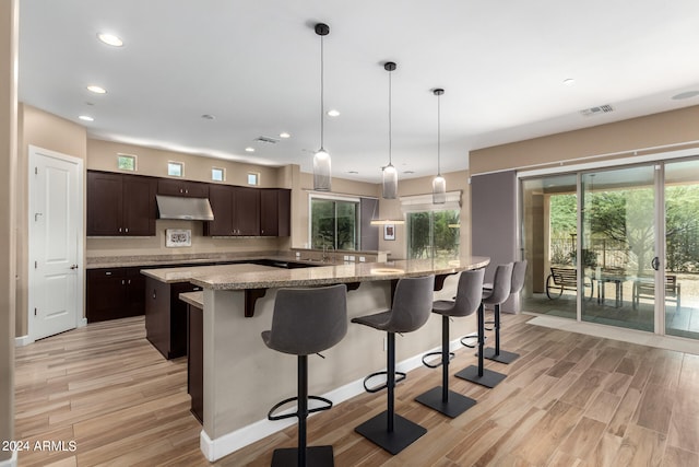 kitchen featuring dark brown cabinets, hanging light fixtures, a kitchen island, light hardwood / wood-style flooring, and light stone countertops