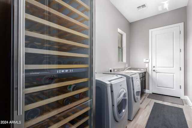 laundry room with washer and clothes dryer, wine cooler, light wood-type flooring, and sink