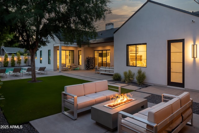 back house at dusk featuring a patio and an outdoor living space with a fire pit