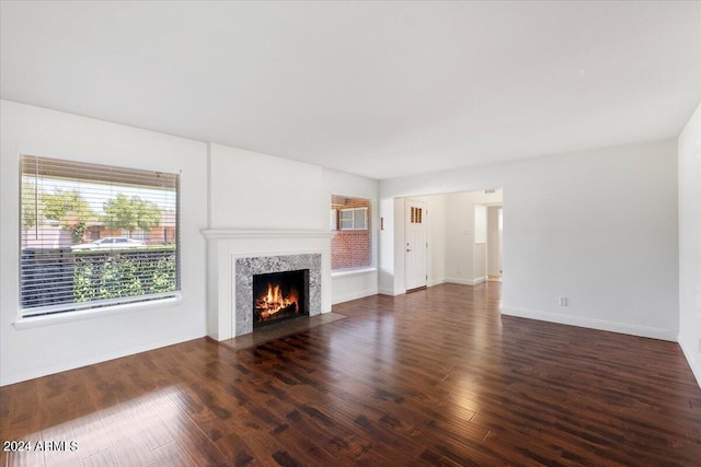 unfurnished living room with dark wood-type flooring, a high end fireplace, and baseboards