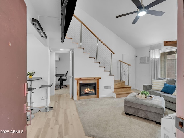 living area with visible vents, a ceiling fan, stairs, and wood finished floors