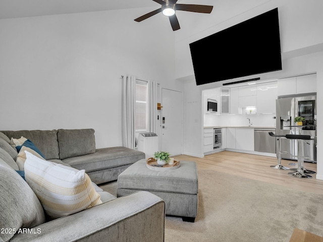 living area featuring light carpet, beverage cooler, a high ceiling, a ceiling fan, and light wood finished floors