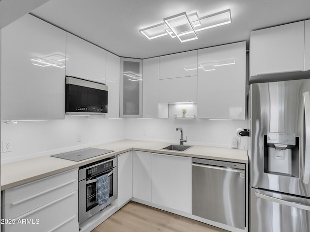 kitchen featuring modern cabinets, white cabinetry, a sink, stainless steel appliances, and light wood-style flooring