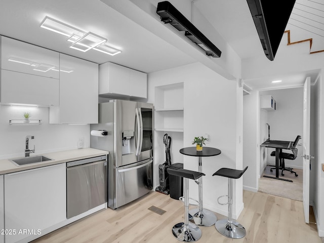 kitchen with a sink, light wood-style flooring, stainless steel appliances, white cabinetry, and modern cabinets