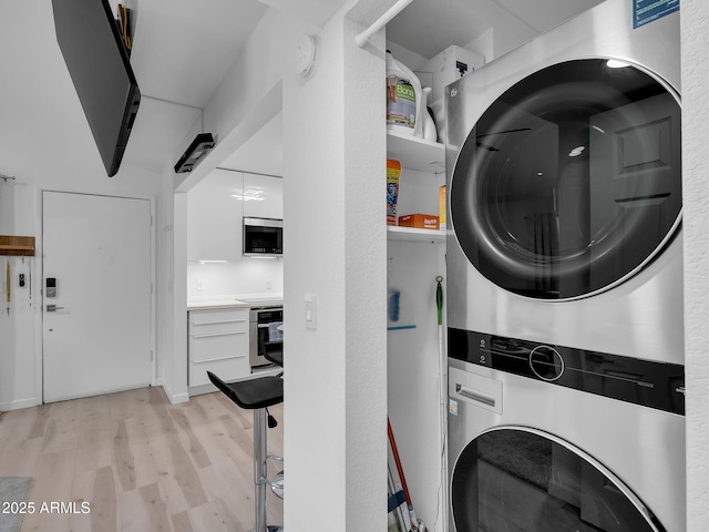 laundry area featuring laundry area, light wood finished floors, and stacked washer / drying machine