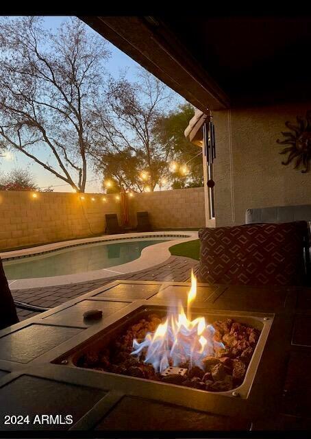 patio terrace at dusk with a fenced backyard, a fire pit, and a fenced in pool