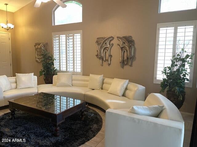 tiled living room featuring ceiling fan with notable chandelier, a towering ceiling, and a healthy amount of sunlight