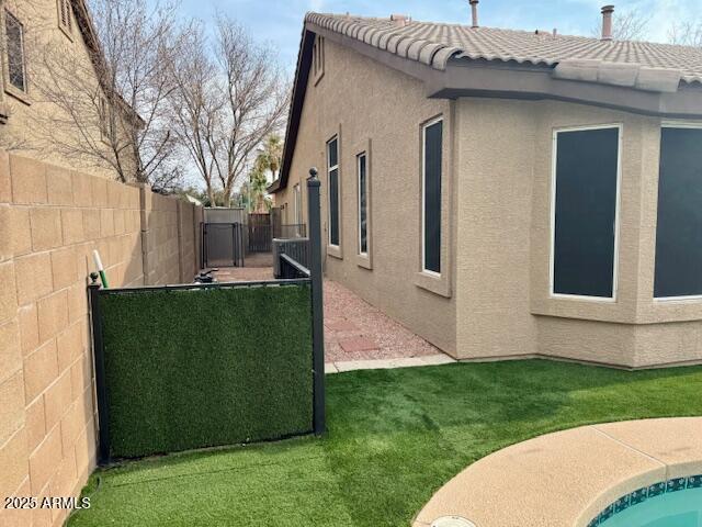 view of home's exterior with a tile roof, a yard, stucco siding, a gate, and a fenced backyard