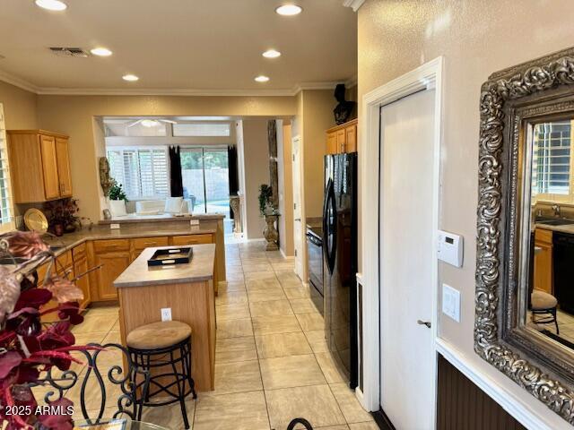 kitchen with a kitchen island, visible vents, light countertops, black appliances, and crown molding