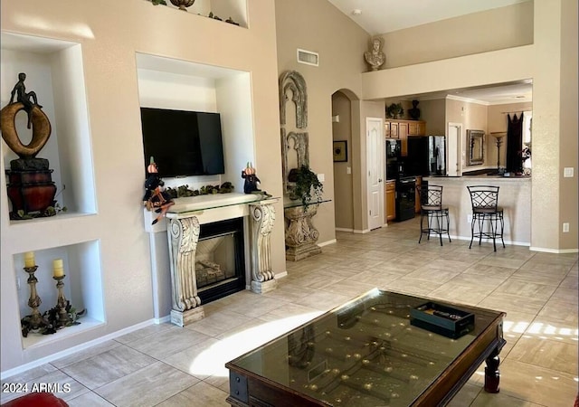 living area with arched walkways, lofted ceiling, visible vents, a glass covered fireplace, and baseboards