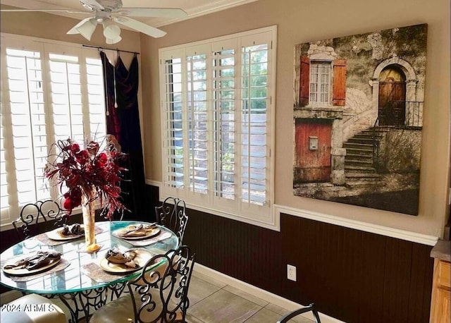 tiled dining space with ceiling fan, wood walls, and ornamental molding