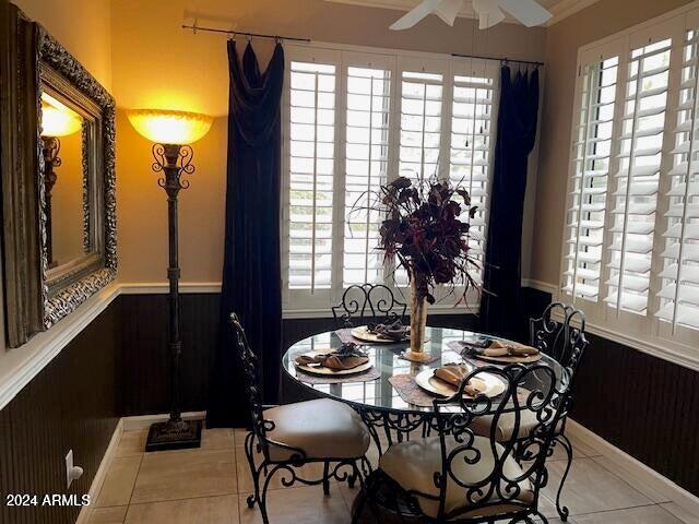 dining space featuring light tile patterned floors, wood walls, wainscoting, and a ceiling fan