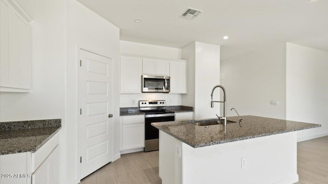 653 W Freedom St, Florence, AZ 85132 - kitchen with appliances with stainless steel finishes, dark stone countertops, a center island with sink, white cabinetry, and recessed lighting