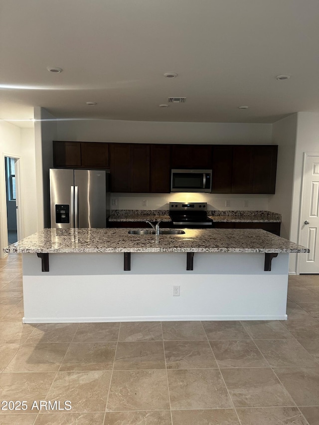 kitchen with light stone counters, appliances with stainless steel finishes, a kitchen bar, and an island with sink