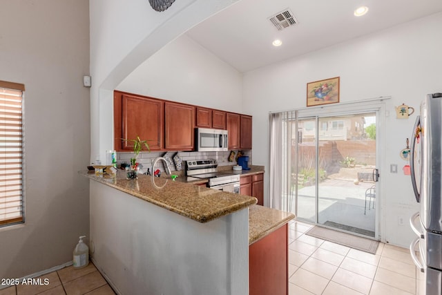 kitchen featuring stainless steel appliances, a high ceiling, light tile patterned floors, brown cabinets, and light stone countertops