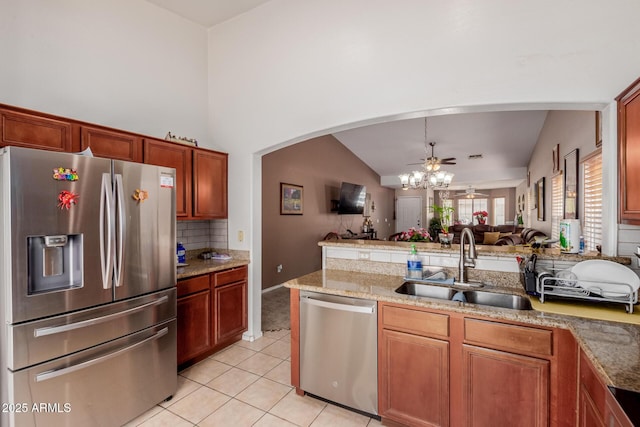 kitchen with stainless steel appliances, open floor plan, a sink, light tile patterned floors, and arched walkways