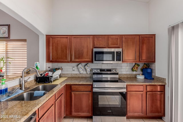 kitchen with appliances with stainless steel finishes, a sink, a high ceiling, tasteful backsplash, and light stone countertops