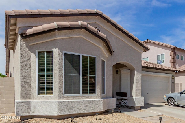 view of front of house with concrete driveway, a tiled roof, an attached garage, and stucco siding