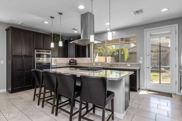 kitchen featuring light tile patterned flooring, a center island, appliances with stainless steel finishes, pendant lighting, and light stone countertops