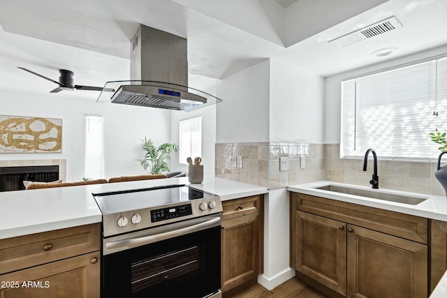 kitchen featuring island exhaust hood, stainless steel electric stove, light countertops, a sink, and a tile fireplace