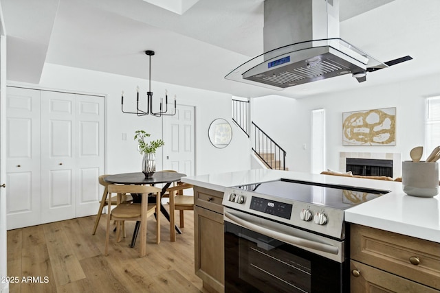 kitchen featuring island range hood, light wood-style floors, light countertops, stainless steel electric range, and decorative light fixtures