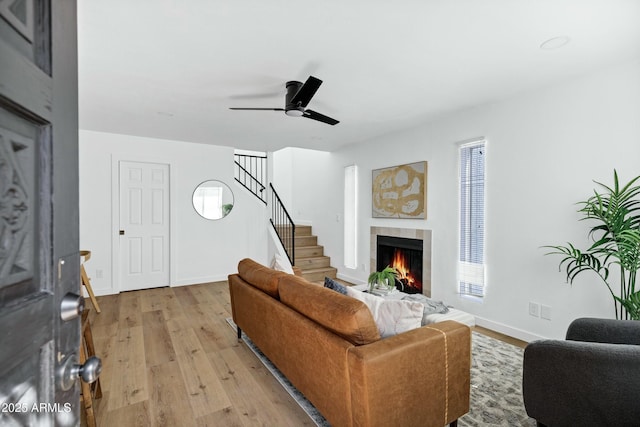 living area with baseboards, stairway, a tiled fireplace, and light wood finished floors