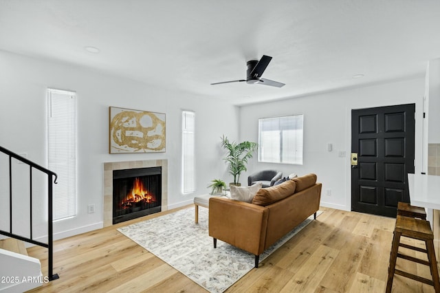 living room featuring light wood finished floors, baseboards, a ceiling fan, and a tile fireplace