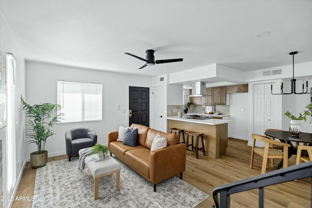 living area with light wood finished floors, baseboards, visible vents, and a ceiling fan