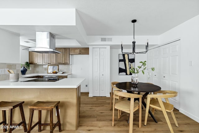 kitchen featuring a peninsula, island exhaust hood, visible vents, and light countertops