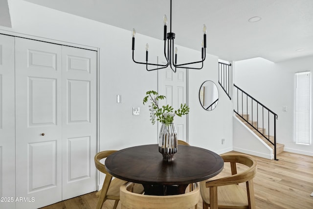 dining space featuring light wood-style floors, stairs, baseboards, and a chandelier