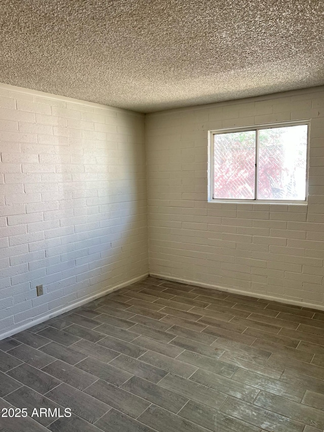 empty room featuring a textured ceiling, dark wood finished floors, and brick wall