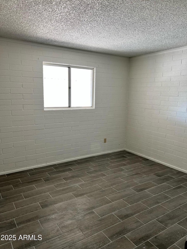 empty room featuring a textured ceiling, wood finish floors, and brick wall