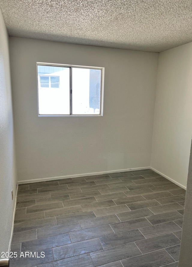 unfurnished room featuring a textured ceiling, wood finish floors, and baseboards