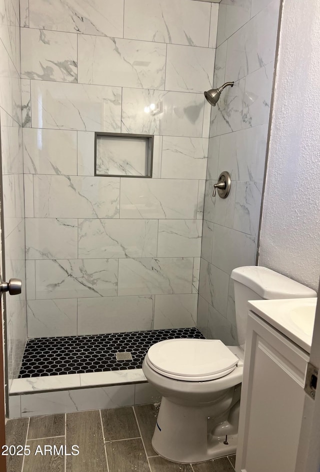 bathroom featuring vanity, a tile shower, and toilet