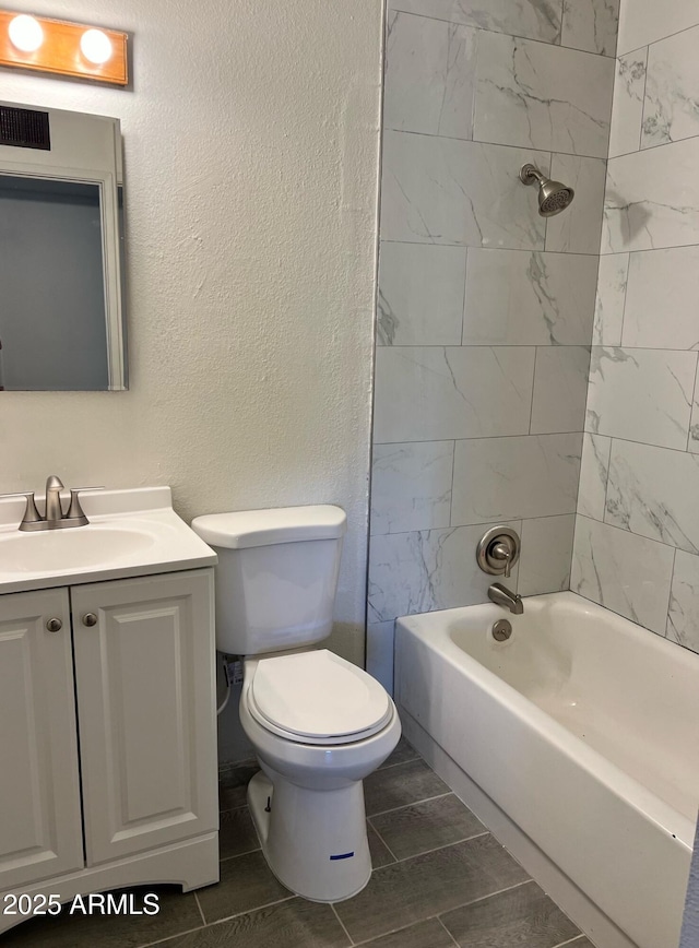 bathroom with vanity, a textured wall, toilet, and shower / washtub combination