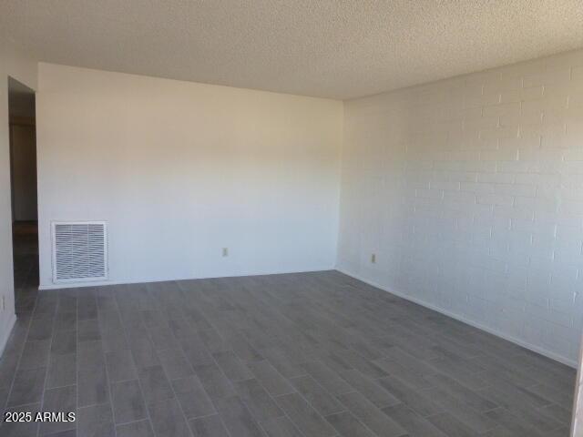empty room with dark wood-style flooring, a textured ceiling, and visible vents