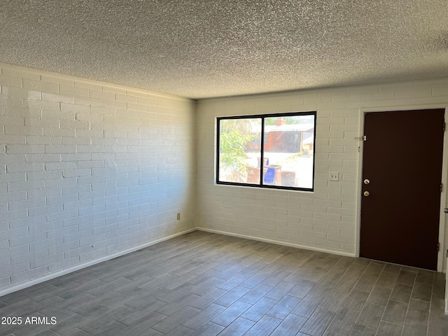 unfurnished room with a textured ceiling, dark wood finished floors, baseboards, and brick wall