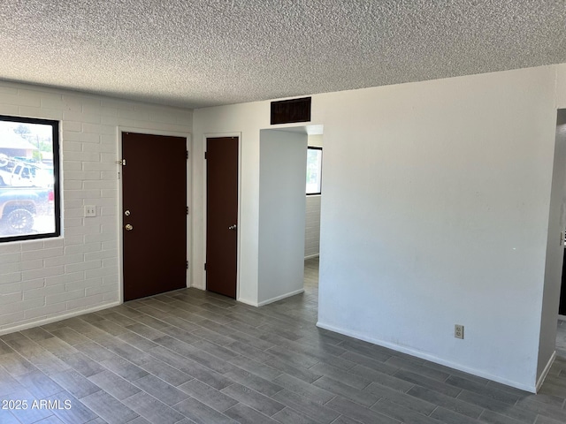 unfurnished room featuring a textured ceiling, dark wood finished floors, baseboards, and visible vents