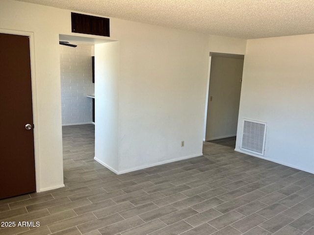 empty room featuring a textured ceiling, visible vents, and wood finished floors