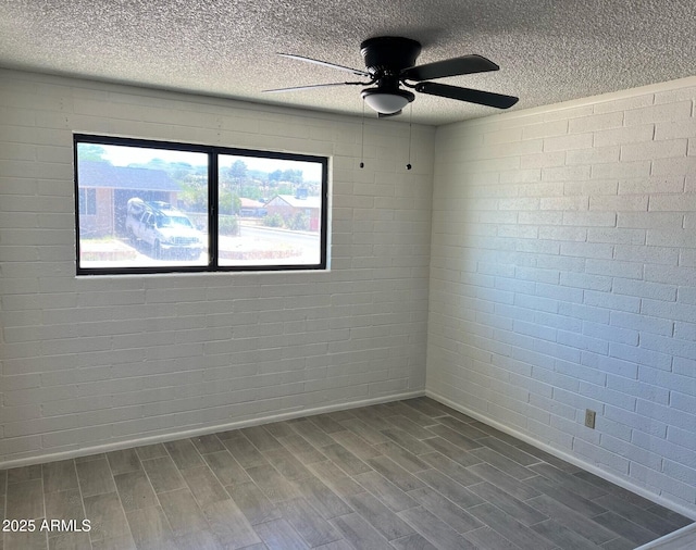 unfurnished room featuring ceiling fan, brick wall, a textured ceiling, baseboards, and dark wood-style floors